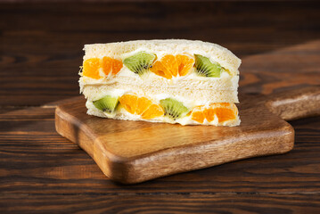 Korean sandwich with kiwi, orange and cream cheese on a wooden board. Hard light. Asian dessert, street food.