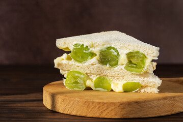 Korean sandwich with green grape and cream cheese on a wooden board. Hard light. Asian dessert, street food.