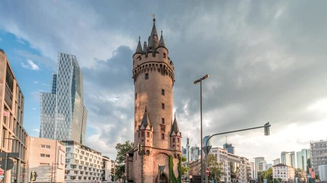 The Eschenheim Tower timelapse hyperlapse. Historic city gate in Frankfurt, Germany. Landmark with modern skyscrapers and busy intersection, the blend of medieval heritage and contemporary urban life