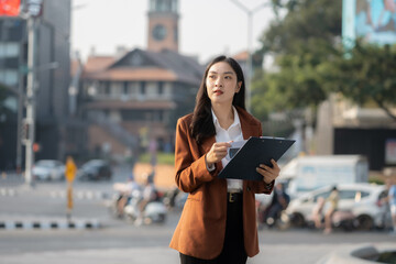 Fototapeta premium Portrait of a successful business woman using smartphone and digital tablet in front of modern business building.