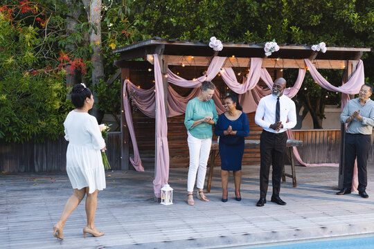 Woman in white dress walking towards smiling senior diverse friends at in garden celebration