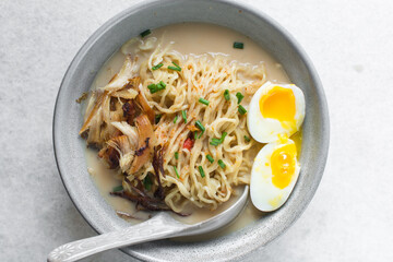 Overhead view of noodles in milk broth in a grey bowl, top view of ramen noodles in creamy chicken broth on a marble countertop