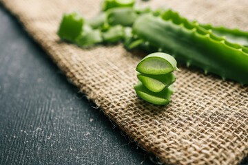 Stacked fresh aloe vera slices on a textured burlap surface. Transparent gel inside the leaves...