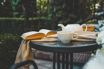 Cozy outdoor scene with a cup of tea, open book, teapot, and a soft scarf on a table. Warm and...