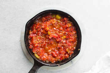 Overhead view of chopped tomatoes and onions in a cast iron skillet, Top view of chopped orange and red tomatoes in a skillet