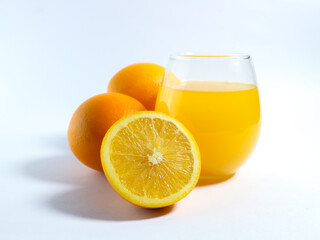 Fresh orange juice in a glass with whole and sliced oranges on a white background