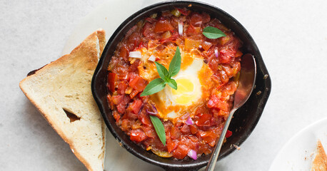 Overhead view of shakshuka in a cast iron skillet, top view of individual Shakshouka in a skillet with a side of toast