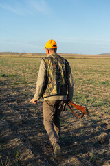 Mature man hunter with gun while walking on field.
