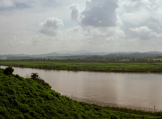 Watchtower Overlooking Serene River And Expansive Green Fields With Rolling Mountains Under Cloudy Sky