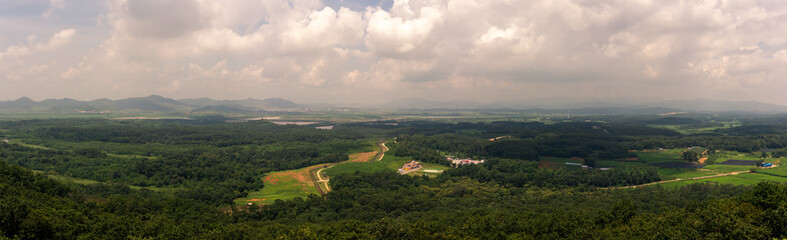 Sweeping Aerial View Of North Korea Green Valleys, Dense Forests, And Rolling Hills Under A Dramatic Cloud-Filled Sky