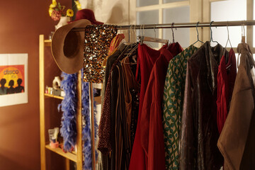 Assorted vintage clothing hanging on rack in a cozy room with decorations and varying textures,...