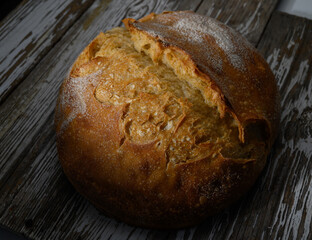 Artisan loaf resting on rustic wooden surface in warm light showcasing its texture and golden crust