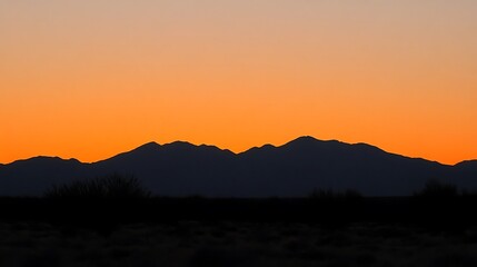 Obraz premium Silhouetted Mountains at Sunset Vibrant Orange Sky