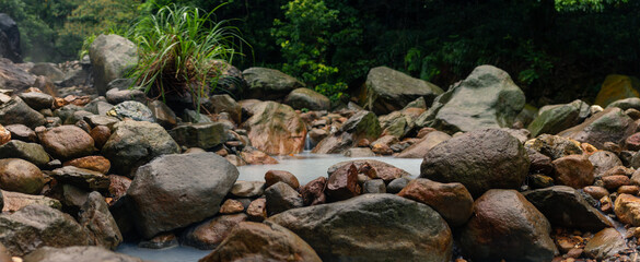 Steaming Natural Hot Spring Flowing Through Rocky Riverbed Surrounded by Lush Greenery in Taiwan