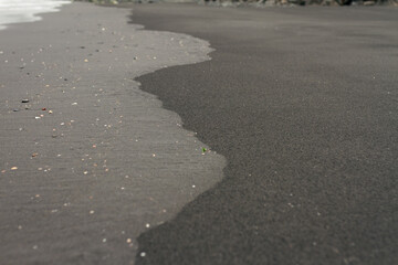 Black volcanic sand shoreline with smooth wet and dry textures forming organic wave patterns along coastline