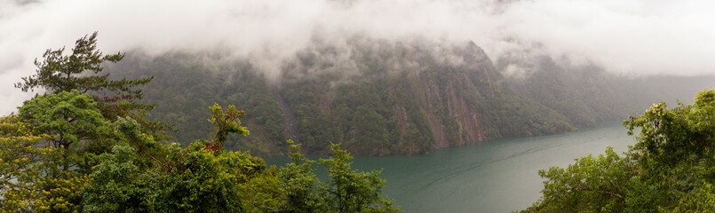 Steep Mist-Covered Mountain Cliffs Overlooking a Serene Emerald Lake Surrounded by Dense Greenery in Taiwan
