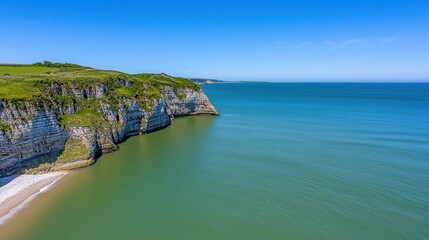 Obraz premium High angle view of a dramatic coastal scene featuring white cliffs, green vegetation, and a calm sea under a bright blue sky. The image showcases the