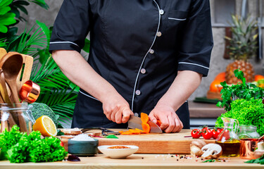 Home Chef cuts carrots. Cozy kitchen with wooden table, kitchenware, vegetables, herbs and ingredients for cooking. Healthy vegan food, culinary, recipes, food blogging