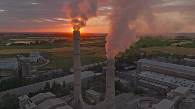 setting sun behind of smoke and steam out of soviet concrete factory pipe, aerial view