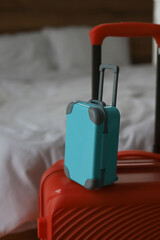 an orange large travel suitcase and along with it a small blue suitcase on the background of a bed with white linens