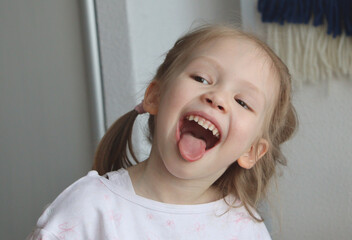 portrait of a little girl with a smile. happy toddler is showing a tongue. 