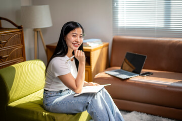 Fototapeta premium A woman sitting on a green couch with a laptop and a pen in her hand