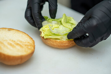 Chef in black gloves preparing gourmet burgers with fresh vegetables and sauce and cutlet in fast food restaurant