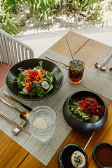 A fresh, healthy meal served outdoors on a wooden table featuring a colorful salad poke bowl iced drink and a soft-boiled egg with elegant tableware and tropical greenery in the background in Maldives