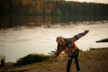 Little girl playing near the lake on an autumn evening. Warm sunset light reflecting on water....