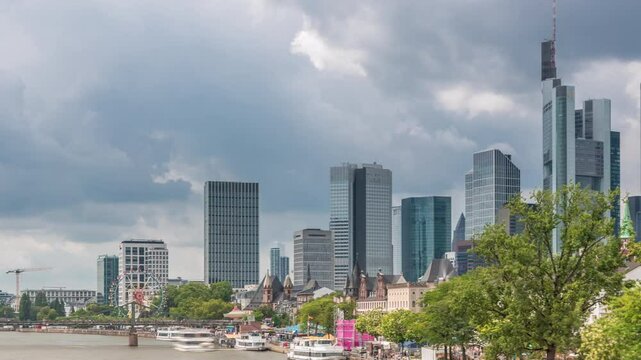 Hyperlapse of the historical Eiserner Steg (Iron Bridge) over the Main River in Frankfurt, Germany. Skyscrapers skyline and waterfront reflect in the water under a cloud-filled sky timelapse