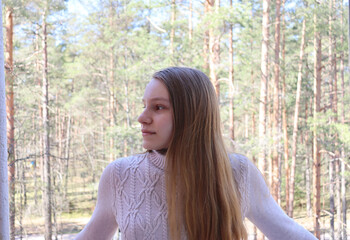 portrait of a young woman in a park. girl standing on a balcony. blond girl in a beige sweater looking aside