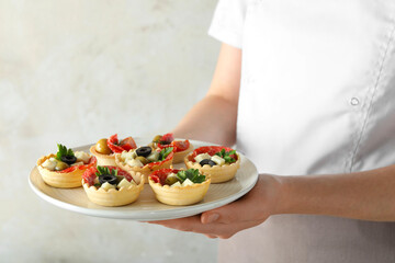 Woman holding plate with tasty canapes on light grey background, closeup
