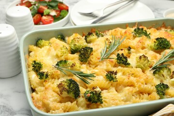 Tasty pasta casserole with cheese, rosemary and broccoli in baking dish on white marble table, closeup