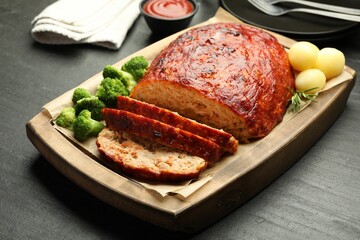 Delicious turkey meatloaf with vegetables served on black table, closeup