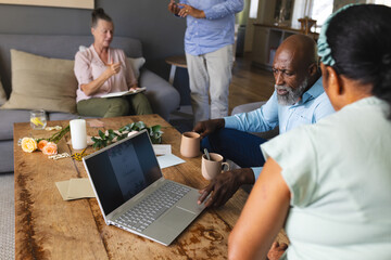 Seniors enjoying coffee and conversation while browsing laptop at home