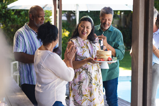 Celebrating birthday outdoors, diverse senior friends smiling joyfully, woman holding cake with cand