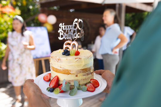 Celebrating 60th birthday with cake and diverse senior friends outdoors in sunny garden