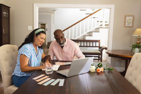 African American senior diverse couple planning home renovation using laptop at dining table