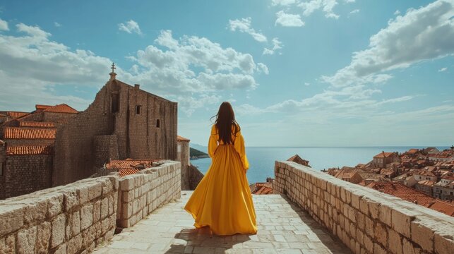 woman in yellow dress on ancient city walls overlooking the sea - Powered by Adobe