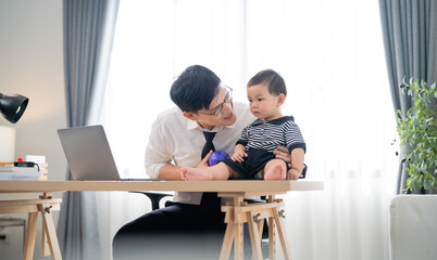 Father playing with baby at home workstation during daytime while working remotely in a modern and cozy environment