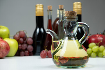 Apple cider vinegar in a vinegar cruet with spout on the background of other types of vinegars and fruits.