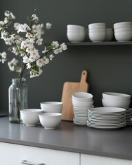 A sleek, modern kitchen with a minimalist aesthetic, featuring dark cabinetry, warm lighting, and neatly arranged white tableware on the counter.  