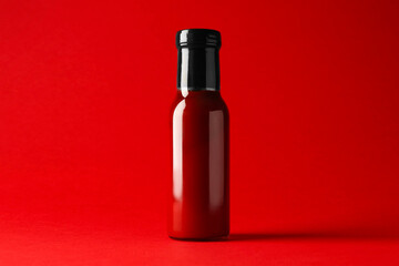 Ketchup in glass bottle on red background