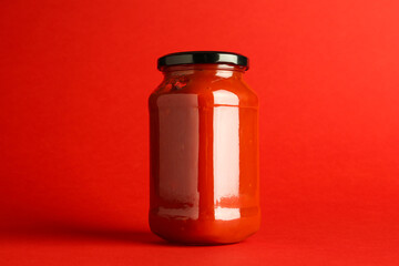 Ketchup in glass jar on red background