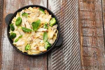 Delicious pasta Alfredo with chicken, cheese, creamy sauce, broccoli and basil on wooden table, top view. Space for text