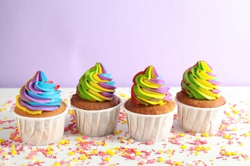 Delicious cupcakes with colorful cream and sprinkles on white wooden table against violet background