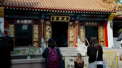 Praying in Chinese temple in Hong Kong, unrecognizable asian people pray with burning sticks. Confucian religion in China, local culture and traditions. Translation: saints and spirits united