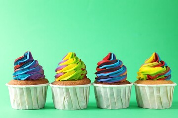 Delicious cupcakes with colorful cream on green background, closeup