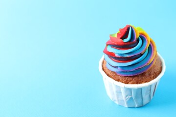 One delicious cupcake with colorful cream on light blue background, closeup. Space for text