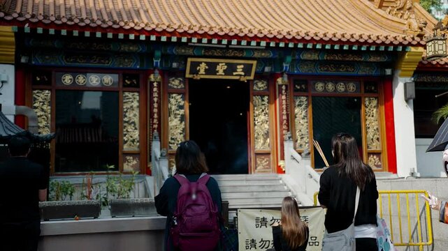 Praying in Chinese temple in Hong Kong, unrecognizable asian people pray with burning sticks. Confucian religion in China, local culture and traditions. Translation: saints and spirits united